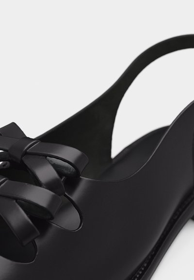 Μαύρο δερμάτινο γόβα με λουράκι και κομψή λεπτομέρεια φιόγκου στο μπροστινό μέρος, με λεία, στρογγυλεμένα άκρα.