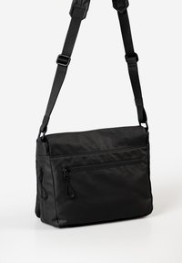 Schwarze Messenger-Tasche aus glattem synthetischem Material, mit verstellbarem Schultergurt, einem Reißverschluss-Vorderfach und boxy Design.