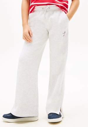 Kind draagt lichtgrijze joggingbroek met zijsplitten en een kleine sterdetail, gecombineerd met marineblauwe sneakers en een roodgestreept shirt.