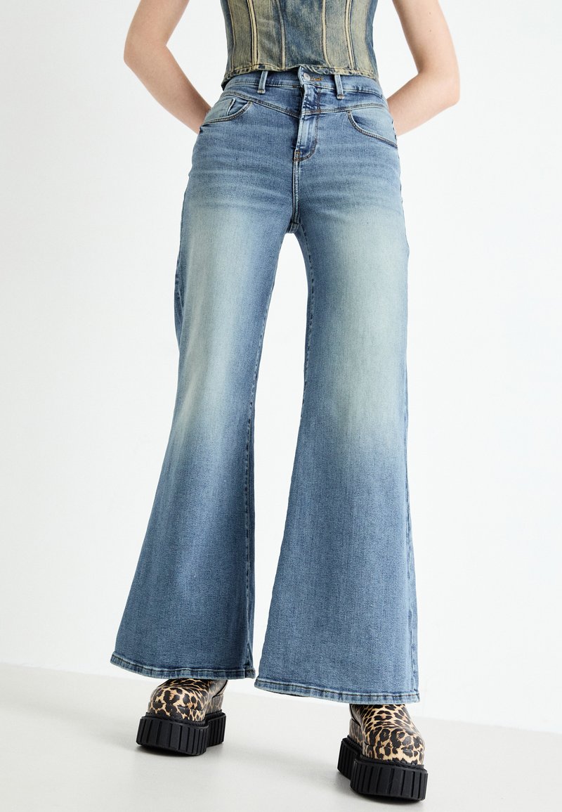 Light blue flared denim jeans with faded accents, a high waist, and five pockets, paired with chunky leopard print platform boots.