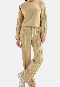 Sweatshirt beige à manches longues et coupe courte, associé à un pantalon assorti avec des rayures verticales et une taille réglable par cordon.