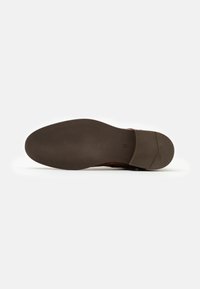 Chaussure en cuir brun avec un dessus lisse et légèrement texturé ; la semelle en caoutchouc présente un motif de crampons pour une meilleure adhérence.