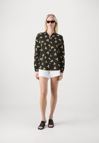 Svart blommig skjorta med gula och vita blommor, bärs med vita slitna shorts och svarta öppna klackskor.