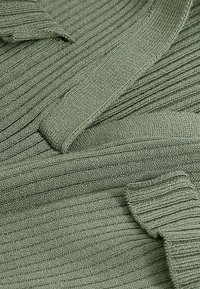 Pull en tricot côtelé de couleur vert doux, avec une texture douce et une coupe classique. Les détails comprennent des manches courbées et un design sans coutures.