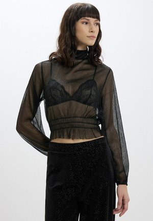 Top lungo a maniche nere in rete con collo alto e orlo arricciato. Tessuto trasparente con un leggero brillante, stratificato sopra un bralette nero.