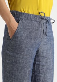Pantaloni in lino blu chiaro con vita regolabile, dotati di tasche laterali e una finitura testurizzata. Tessuto morbido con leggere variazioni.