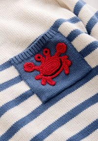 Tissu tricoté rayé bleu et blanc avec un emblème de crabe rouge au crochet cousu sur un patch carré bleu uni.