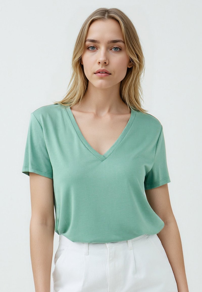 T-shirt verde a V in tessuto leggero con maniche corte, abbinato a pantaloni bianchi a vita alta, caratterizzati da una vestibilità rilassata.