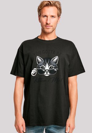 Black cotton t-shirt featuring a kitten graphic with sunglasses, accompanied by the text "YOU GOTTA BE Kitten Me!" in a playful font.