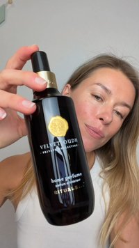 Czarna szklana butelka perfum z złotą nakrętką i emblematem. Etykieta z napisem „Velvet Oudh, perfumy do domu, Rituals” w białym kolorze.