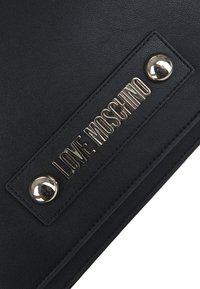 Borsa a tracolla in pelle nera con il nome inciso "LOVE MOSCHINO" in oro metallizzato, accentuata da borchie in tonalità argento e una superficie texturizzata.