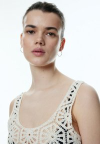 Gehaakte tanktop in crème met ingewikkelde bloemmotieven. Heeft een brede halslijn en bandjes, en laat een gestructureerde afwerking zien.