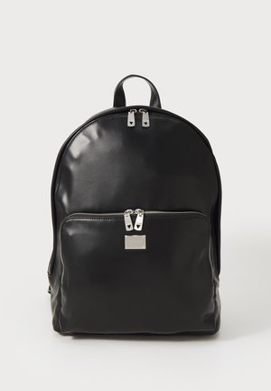 Zaino in pelle nera con una consistenza liscia, forma arrotondata, tasca con zip anteriore e dettagli in metallo argentato. Presenta doppie zip superiori.