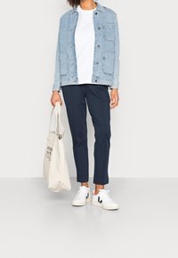 Lyseblå denimjakke, hvid t-shirt, mørkeblå skræddersyede bukser og hvide sneakers med sorte detaljer. Holder en lys beige tote taske.