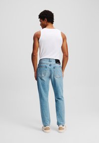 Šviesiai mėlynos džinsinės kelnės tiesaus kirpimo, su penkių kišenių dizainu ir kontrastingomis siūlėmis. Dėvimos su baltu topu be rankovių ir kasdieneis batais.