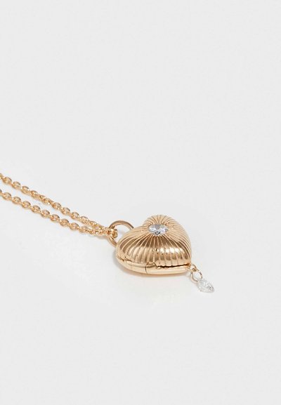 Zlati locket v obliki srca z rebrasto zasnovo, ki vsebuje prozoren kamen in viseči kapljični detajl. Pritrjen na fino verigo.