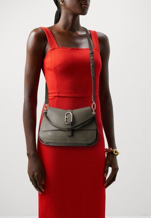 Sac en cuir gris à bandoulière avec une fermeture à rabat, quincaillerie argentée et une sangle réglable, porté sur une robe rouge à texture.