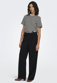 Sort og hvid stribet t-shirt kombineret med sorte bukser med vide ben og knapper foran, suppleret med brune blokhælede sko.