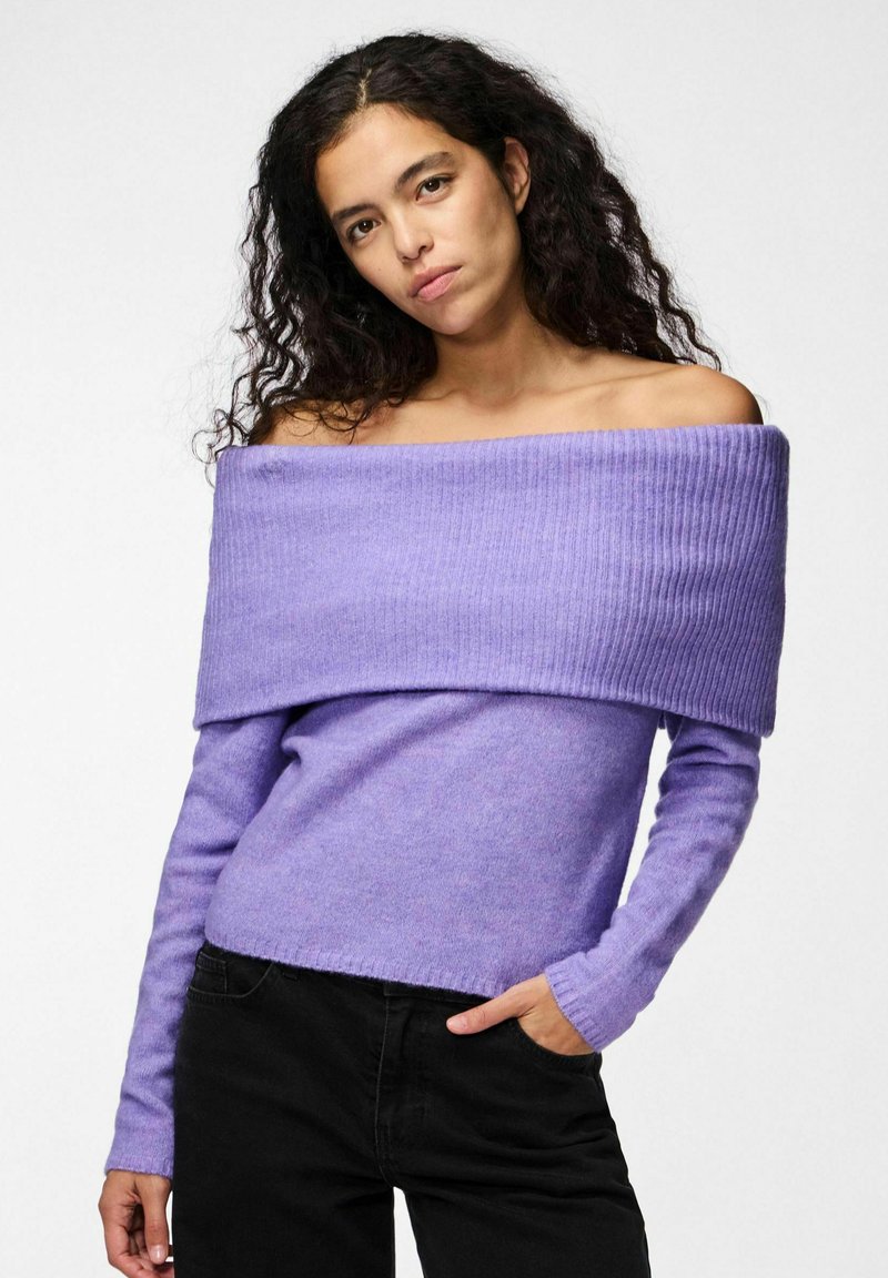 Maglione viola con spalle scoperte, colletto a costine e maniche lunghe, realizzato in tessuto morbido, abbinato a pantaloni neri.