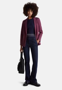 Vínové sako přes námořnicky modrý žebrovaný svetr, kombinované s tmavými rozšířenými džínami. Černá kabelka v ruce a černé boty doplňují vzhled.