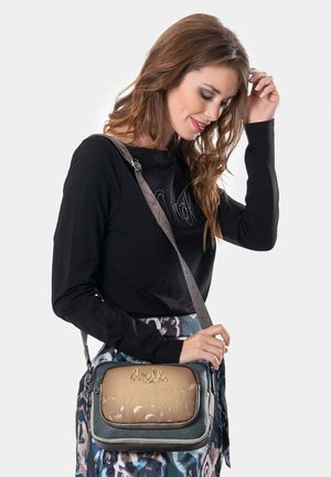 Umhängetasche mit einem tanfarbenen und grauen Design, das florale Prägungen und ein metallisches Logo aufweist. Verstellbarer Riemen und Reißverschluss. 