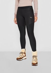 Svarta leggings med en slank design, med hög midja, kontrasterande paneler och en logotyp. Bärs med tanfärgade vinterstövlar foder med konstpäls.