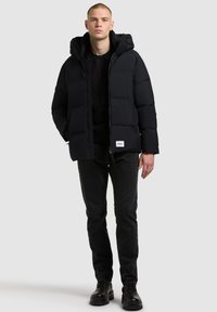 Must must vest, mille kaelusega, millel on lõppfront ja logo plekk. Kandmine musta sviitri peal ja koos tumeda teksadega ning saabastega.