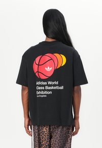 Svart kortermet T-skjorte med tre overlappende basketballgrafikker i rødt, oransje og gult, med teksten "Adidas World Class Basketball Exhibition".