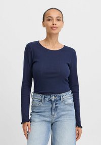 Marineblaues Langarmoberteil aus geripptem Material mit Rundhalsausschnitt. Kombiniert mit hoch geschnittenen Jeans aus hellblauem Denim mit fransigem Saum.