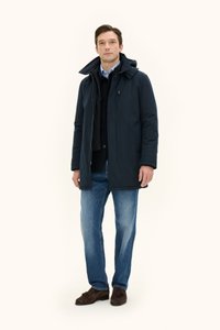 Tummansininen pehmeä takki, jossa on korkea kaulus ja huppu, mustan neuleen päällä, vaaleansiniset farkut ja ruskeat mokkakengät.