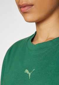 Vihreä puuvillainen t-paita, jossa on pyöreä pääntie, ja vasemmalla puolella pääntien läheisyydessä vaalea vihreä Puma-logo.