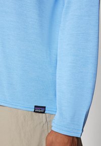 Light blue long-sleeve shirt made of soft, textured fabric. Features a stitched hem and a black Patagonia label at the bottom left.
