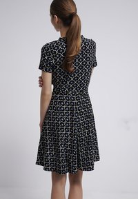 Svart klänning med mönstrad design i blått och vitt, korta ärmar, åtstramad midja och utsvängd kjol. Slät tygtextur.