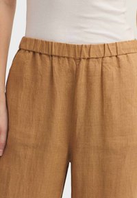 Pantalon en lin brun avec une taille élastique, présentant une coupe ample et une texture subtile. Aucune couture ni poche visible n'est apparente.