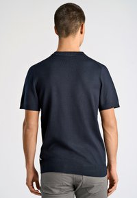 Mörkblå kortärmad polo med en strukturerad stickad mönster, ribbad krage och manschetter, sidofickor och en diskret logotypsaccent.