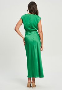 Green satin maxi dress with cap sleeves, fitted waist, and a smooth texture. It features a simple back closure and a flowing silhouette.