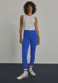 Leggings azules acanalados con una cinturilla alta y un acabado suave, combinados con una camiseta sin mangas blanca ajustada y zapatillas plateadas.