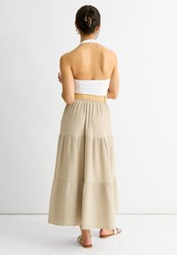 Gonna maxi a strati beige realizzata in tessuto testurizzato, conampia vita elasticizzata e design fluido. Semplice e traspirante.