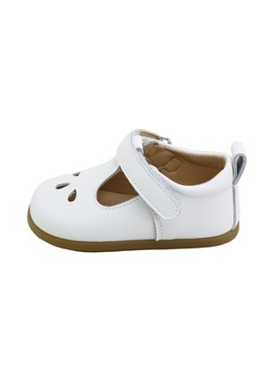 Zapato blanco para niño pequeño con tira de velcro, recortes en forma de gota en la parte superior, suela marrón claro y forro interior suave color canela sobre fondo blanco.