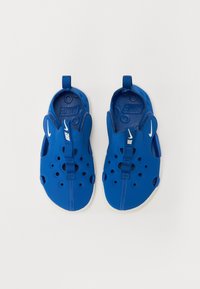 Blå slip-on sko med lett, perforert design, med en stropp og hvite detaljer. Materialet ser gummiaktig ut med en strukturert overflate.