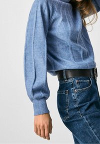 Jasnoniebieski sweter z prążkowanej dzianiny, z długimi, lekko bufiastymi rękawami i okrągłym dekoltem, zestawiony z ciemnoniebieskimi dżinsami.