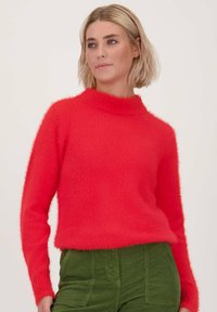 Rode harige gebreide trui met een hoge hals en lange mouwen, gecombineerd met groene corduroypantalons. De textuur lijkt zacht en warm.