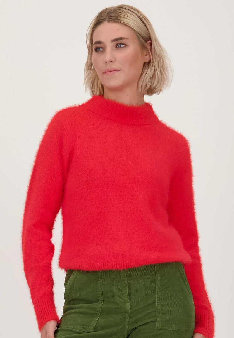 Rode harige gebreide trui met een hoge hals en lange mouwen, gecombineerd met groene corduroypantalons. De textuur lijkt zacht en warm.