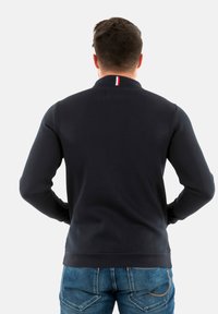 Marine blauwe sweatshirt met een hoge kraag, ribgebreide manchetten en onderrand. Heeft een kleine rode, witte en blauwe accent aan de achterkant van de halslijn.