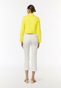 Yellow cropped jacket made of denim with long sleeves and button accents, paired with white cropped pants and beige heeled sandals.