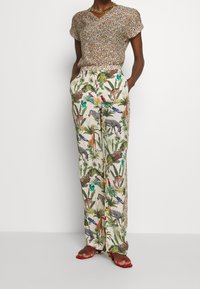 Bluzka z krótkim rękawem w panterkę zestawiona z białymi spodniami w zwierzęcy i tropikalny wzór. Czerwone sandały na płaskiej podeszwie.