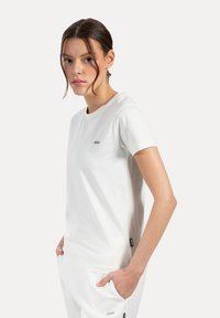 Lettet hvid t-shirt lavet af bomuld, med rund halsudskæring, korte ærmer og et lille logo på forsiden.