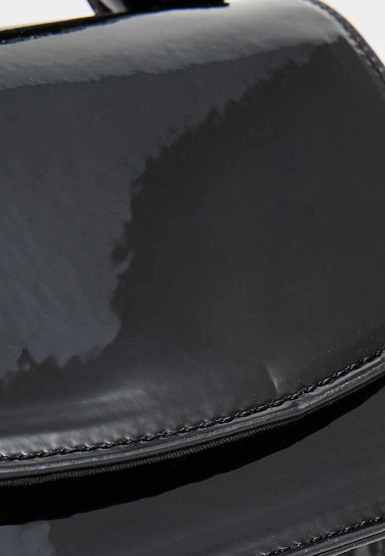 Sac à main en cuir verni noir avec une surface lisse et brillante, forme rectangulaire, fermeture à glissière et un minimum de détails de couture.