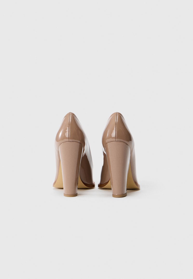 Tacones altos de charol nude con punta afilada y tacón grueso. Textura suave con un acabado brillante y detalles de costura mínimos.