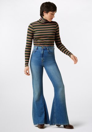 Gestreifter Rollkragenpullover in Schwarz mit mehrfarbigen horizontalen Linien, kombiniert mit hochgeschnittenen blauen Schlagjeans, die weite Beine und einen ausgewaschenen Look aufweisen.